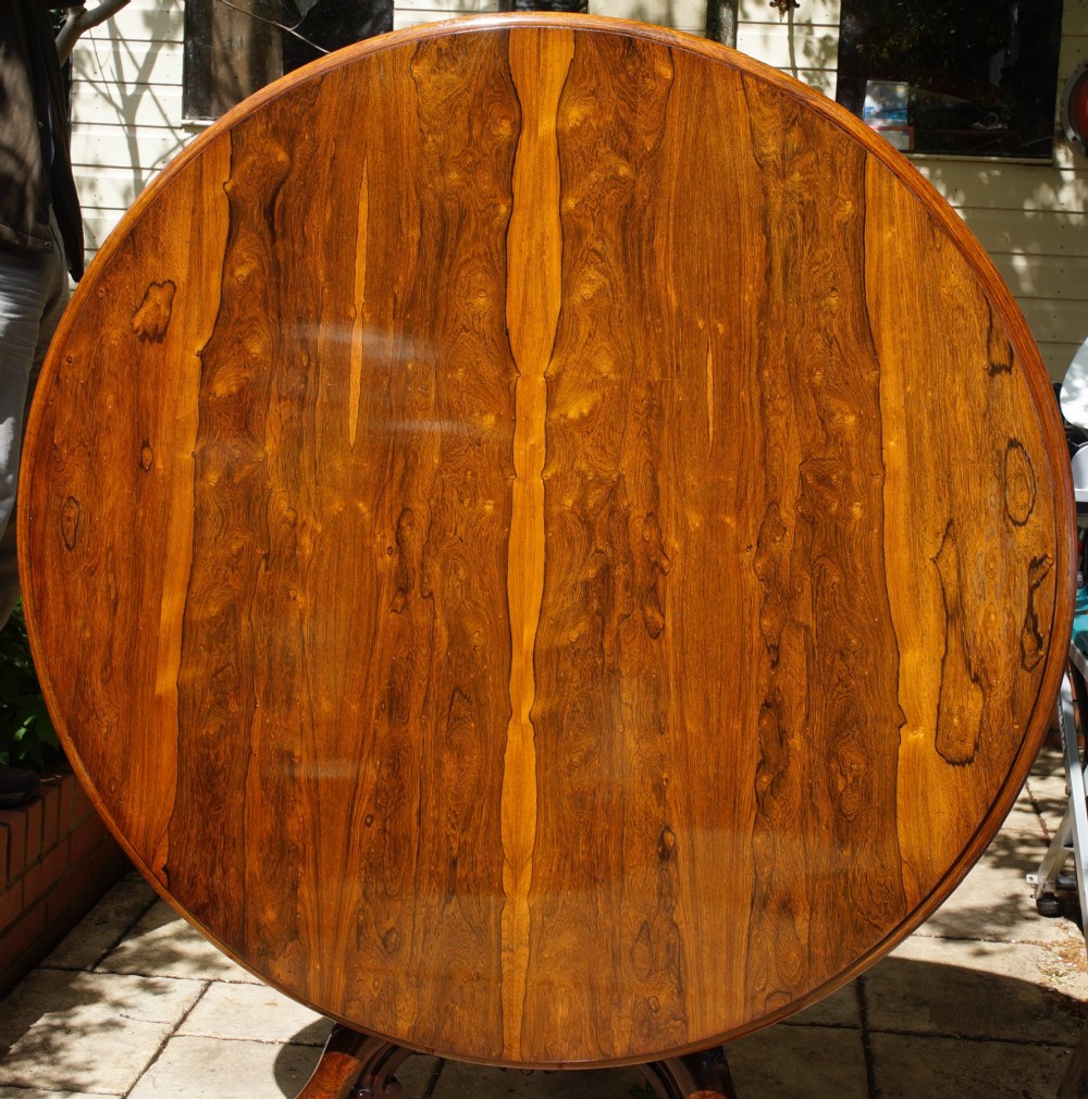 A circular rosewood dining table top exhibiting prominent book-matched grain patterns in shades of warm brown and deep dark brown.