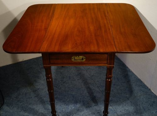 A mahogany Pembroke table featuring two drop leaves, a single frieze drawer with a recessed brass handle, and four turned legs.