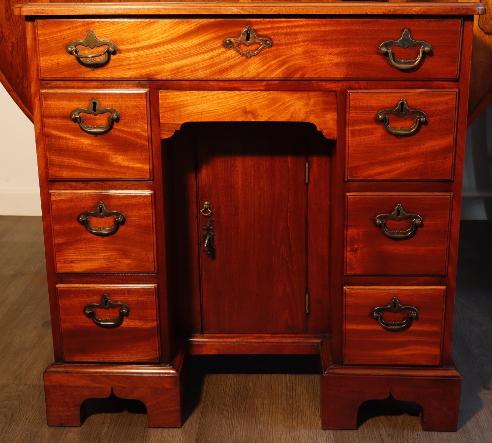 A Georgian mahogany kneehole dressing table featuring multiple drawers with brass swan-neck handles, a recessed central cupboard, and bracket feet.
