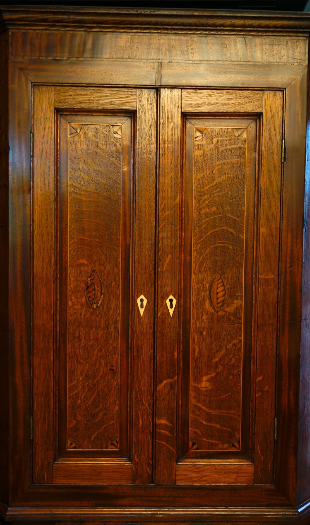 An antique oak hanging corner cupboard with twin panelled doors, inlaid central motifs, bone keyhole escutcheons, and a moulded top cornice. View II