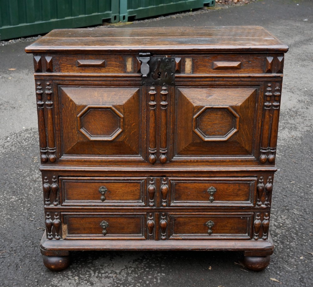 An antique dark oak mule chest featuring geometric fielded panels, turned split-baluster mouldings, lower drawers, and bun feet.