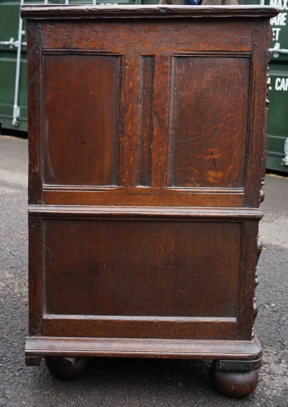 An antique dark oak mule chest featuring geometric fielded panels, turned split-baluster mouldings, lower drawers, and bun feet. View V