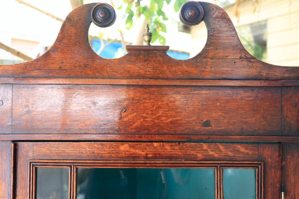 An antique wooden hanging corner cabinet featuring an astragal glazed door, a swan-neck pediment, and a painted teal interior with two shelves. View III