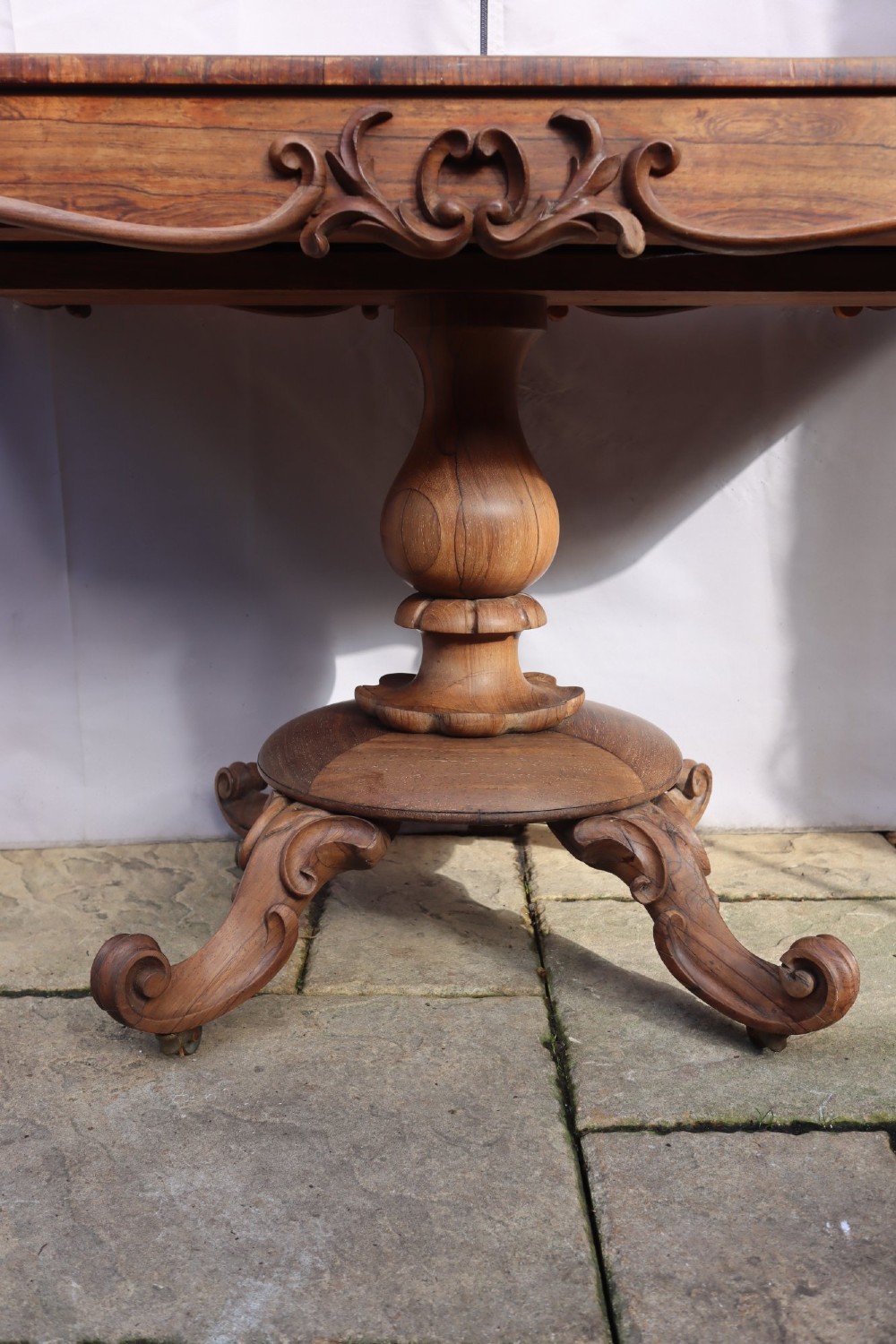 A Victorian rosewood centre table with a rectangular top, carved frieze, a central turned bulbous pedestal, and scroll legs on castors. View II