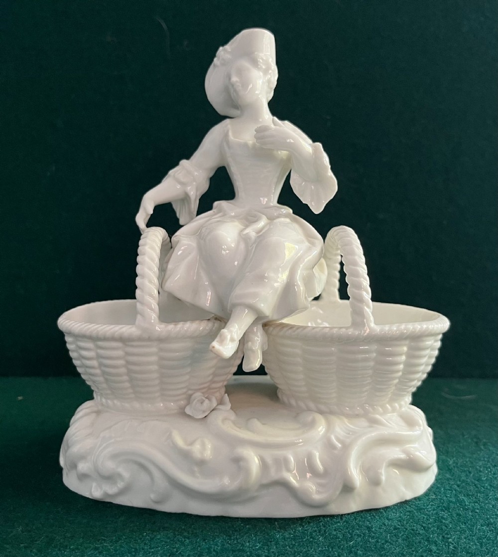 A pair of white glazed porcelain figurines depicting a male and female figure in 18th-century attire, each seated between two woven basket-form dishes on scrollwork bases. View IV