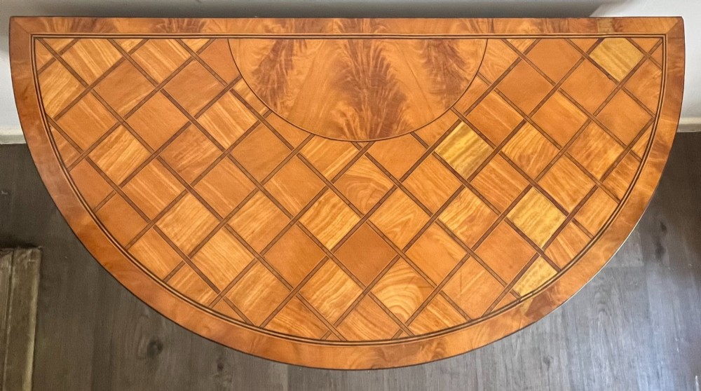 An antique George III demilune card table in honey satinwood featuring geometric parquetry inlay and tapered legs. View II