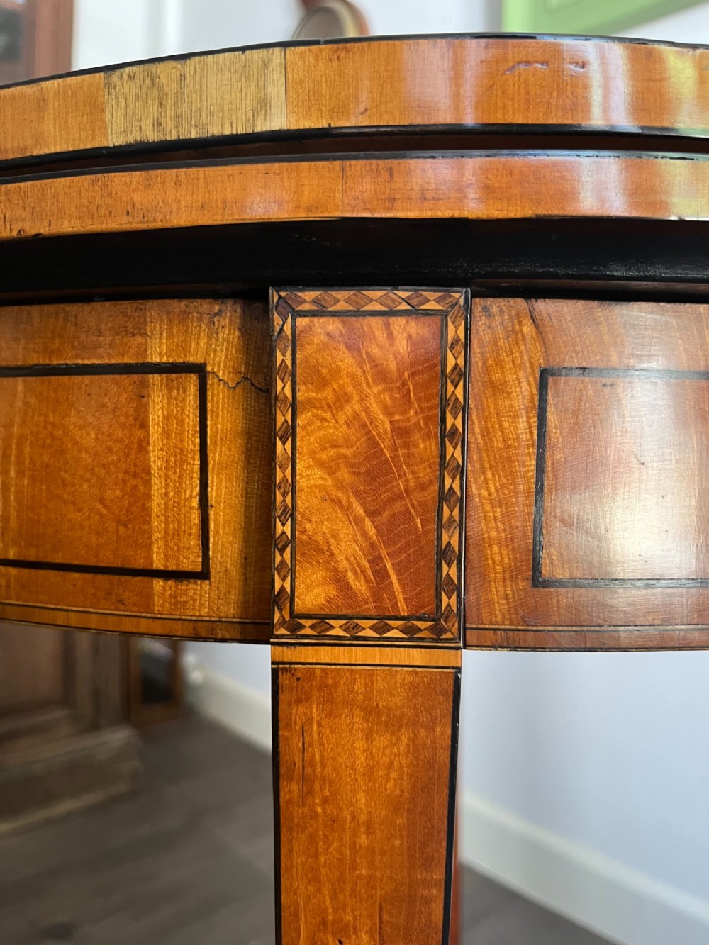 An antique George III demilune card table in honey satinwood featuring geometric parquetry inlay and tapered legs. View V