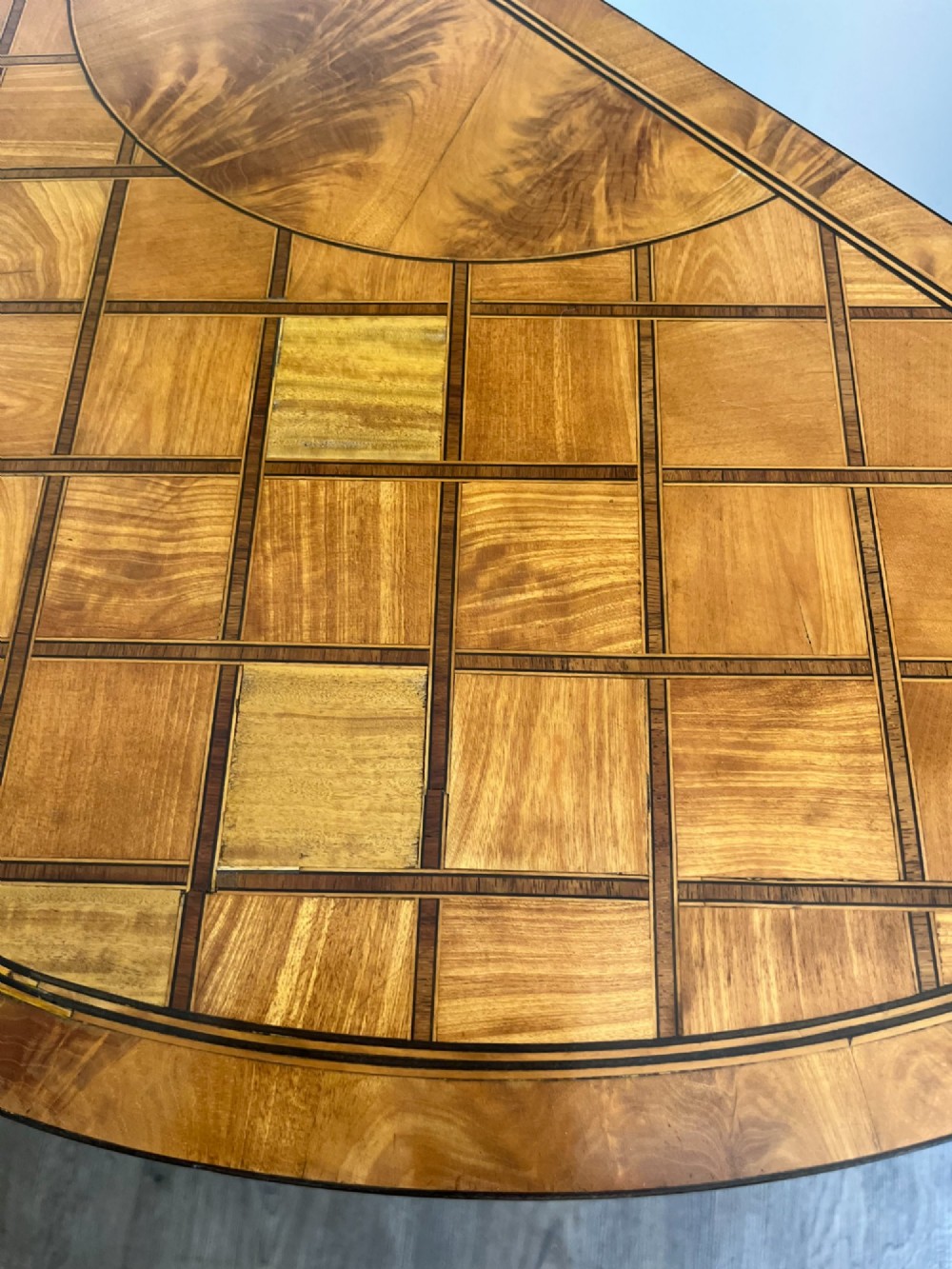 An antique George III demilune card table in honey satinwood featuring geometric parquetry inlay and tapered legs. View VI