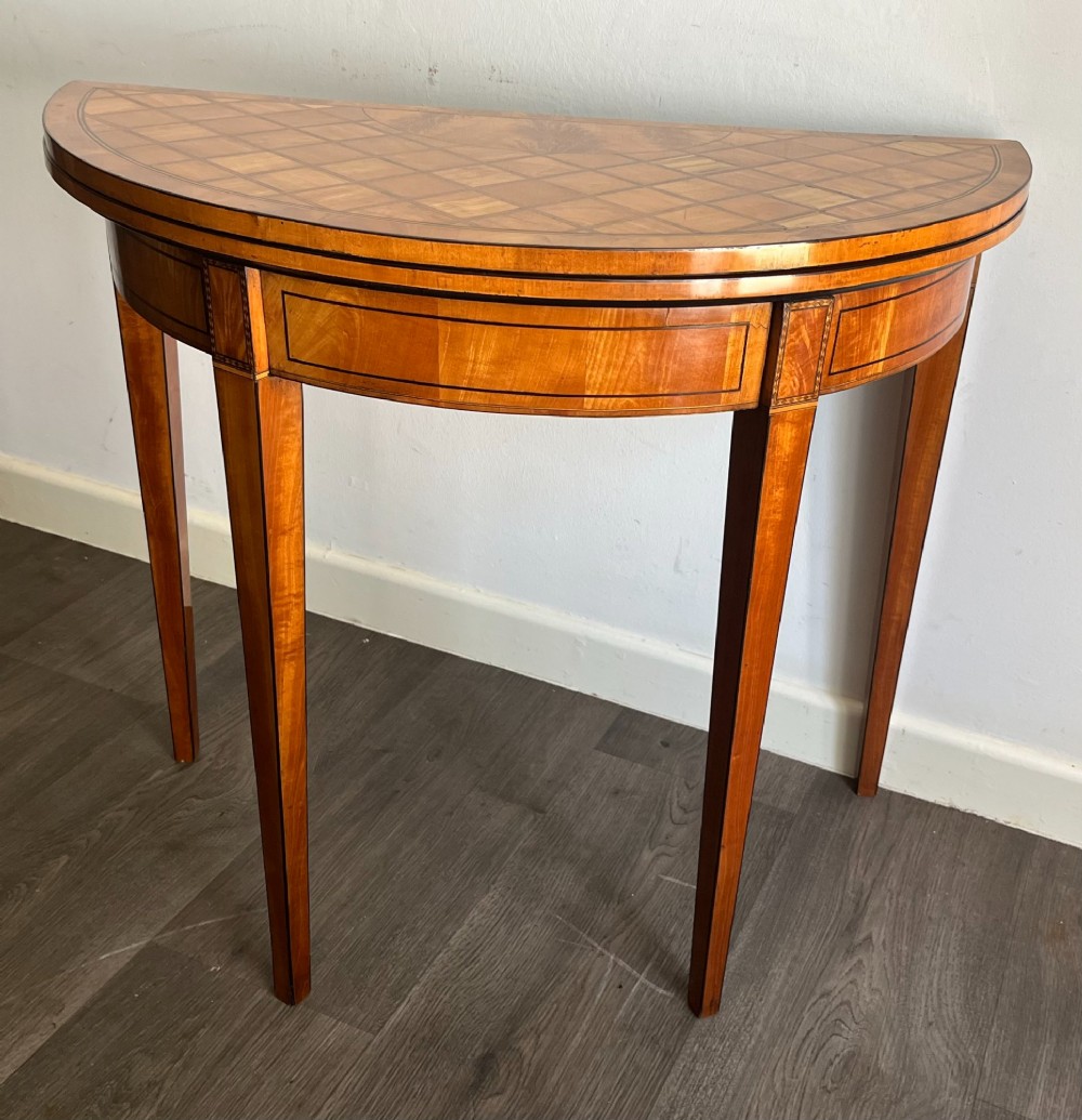 An antique George III demilune card table in honey satinwood featuring geometric parquetry inlay and tapered legs. View IX