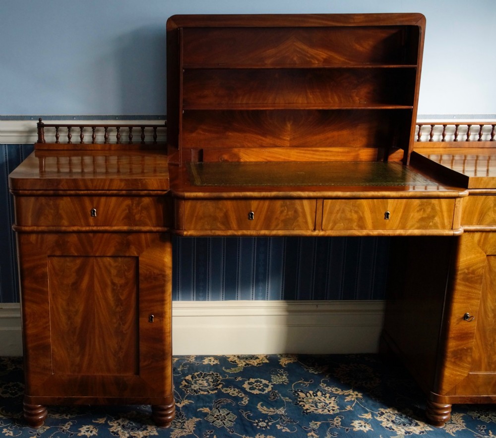 A flame mahogany pedestal desk with a central green leather writing surface, open upper shelf gallery, and turned feet.