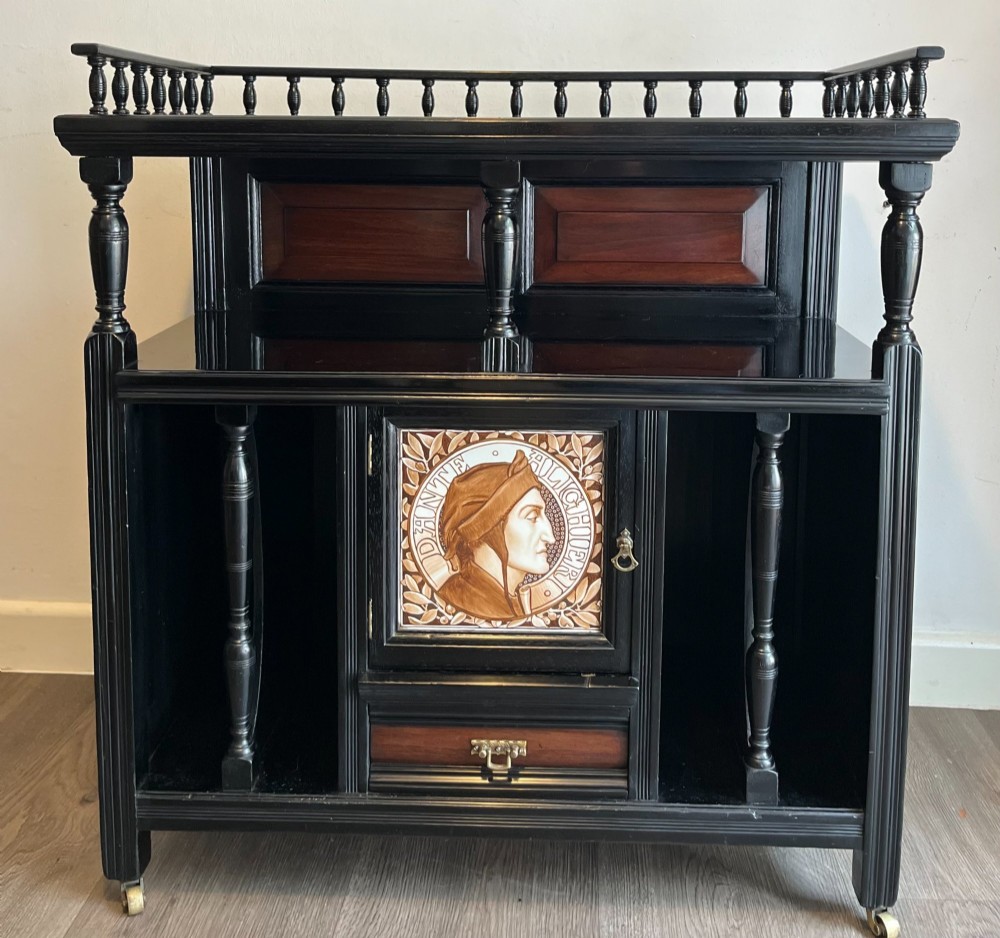 A late Victorian ebonised wood cabinet with a top spindle gallery, dark mahogany panels, and a central door featuring a profile ceramic tile of Dante.