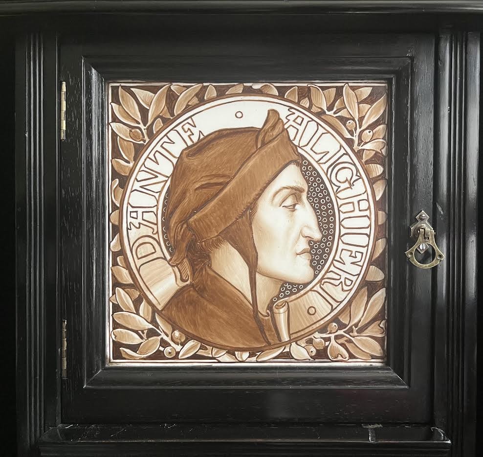 A late Victorian ebonised wood cabinet with a top spindle gallery, dark mahogany panels, and a central door featuring a profile ceramic tile of Dante. View IX