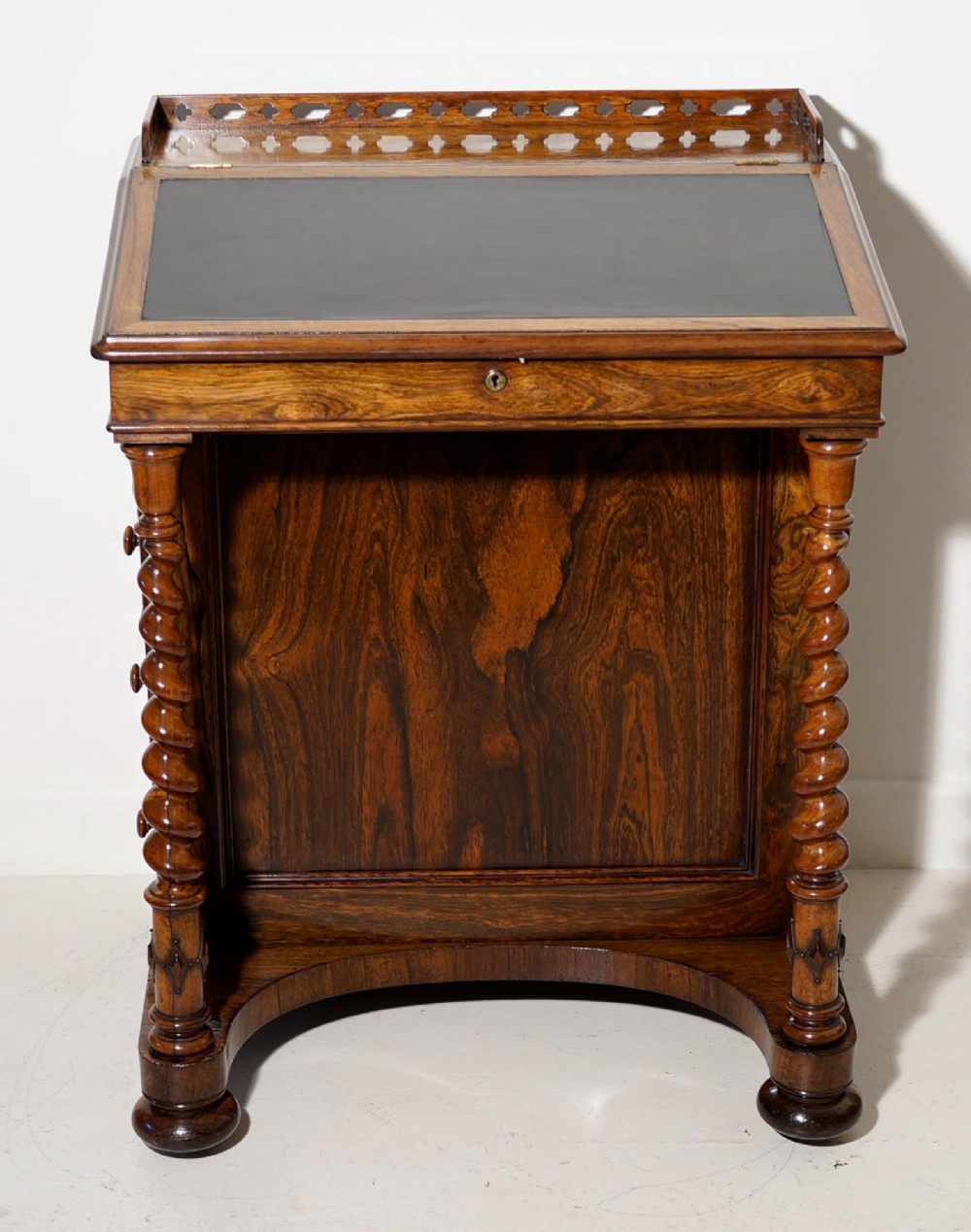 An antique dark rosewood Davenport desk featuring a slanted black leather writing surface, pierced gallery top, side drawers, and turned barley twist front columns.