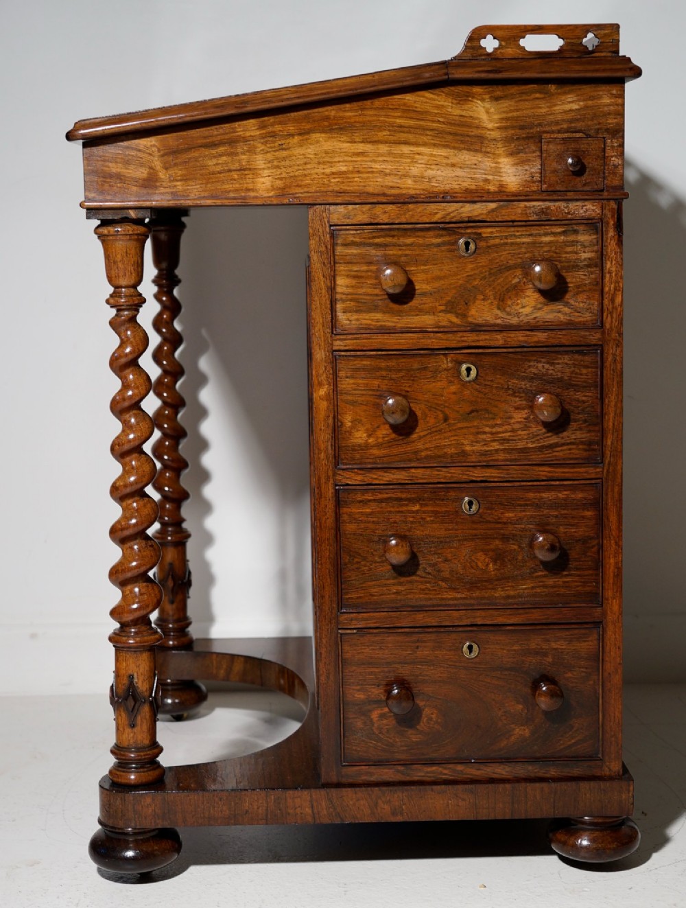 An antique dark rosewood Davenport desk featuring a slanted black leather writing surface, pierced gallery top, side drawers, and turned barley twist front columns. View IV
