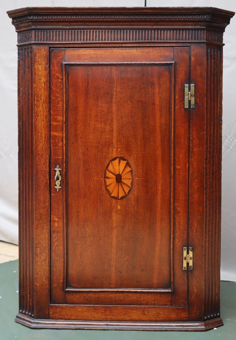 A Georgian mahogany corner cupboard with a single door featuring a central oval starburst inlay and exposed brass H-hinges.