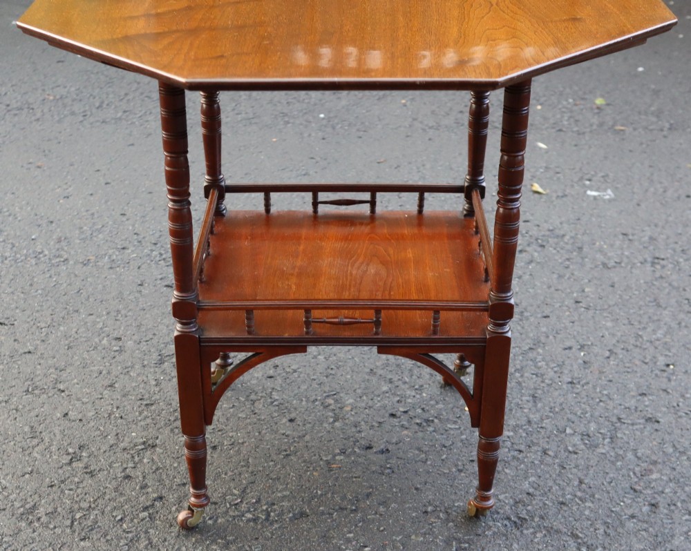 An antique octagonal mahogany occasional table featuring an upper octagonal surface, a lower tier with a spindle gallery, turned legs, and brass castors. View IV