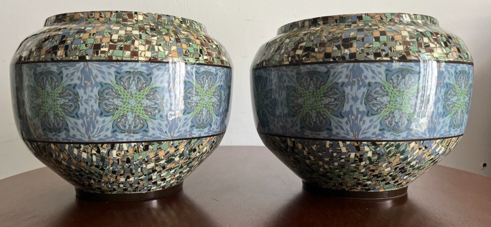 A pair of round ceramic vases with mosaic tile pattern bands around the rim and base and a blue and green stylised floral pattern across the centre.
