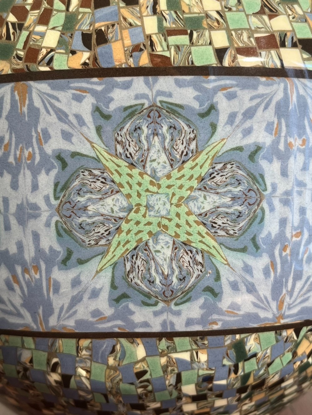 A pair of round ceramic vases with mosaic tile pattern bands around the rim and base and a blue and green stylised floral pattern across the centre. View VI