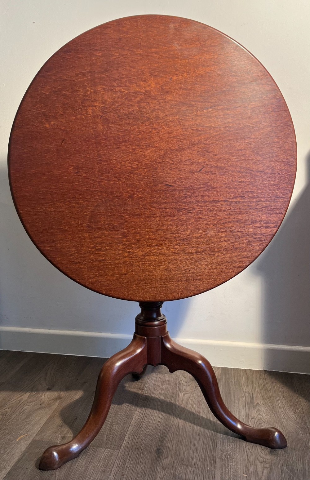 A mahogany tilt-top tripod table shown with its top positioned vertically, revealing a turned central column and cabriole legs. View III