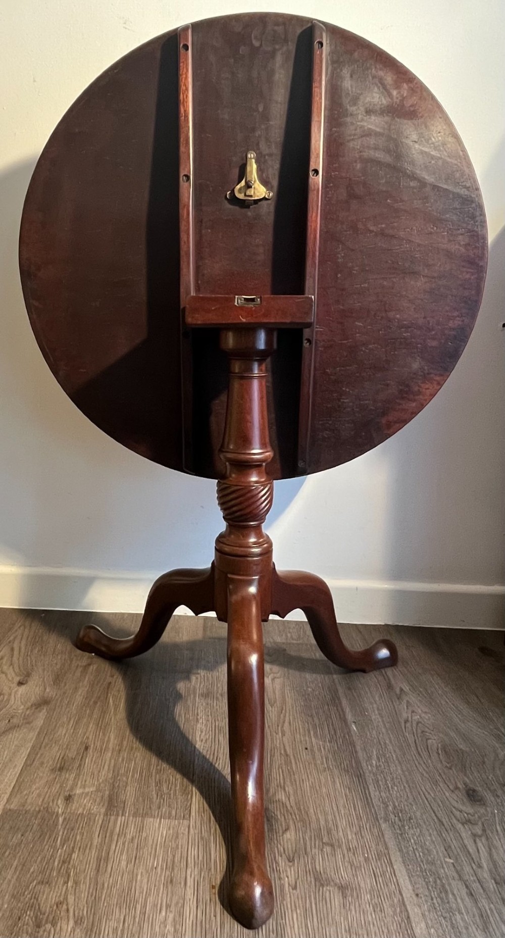 A mahogany tilt-top tripod table shown with its top positioned vertically, revealing a turned central column and cabriole legs. View IV