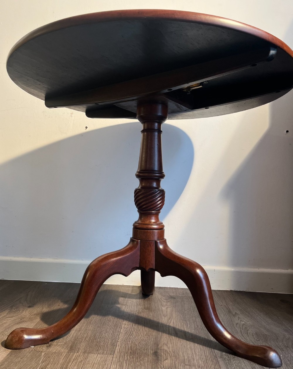 A mahogany tilt-top tripod table shown with its top positioned vertically, revealing a turned central column and cabriole legs. View V