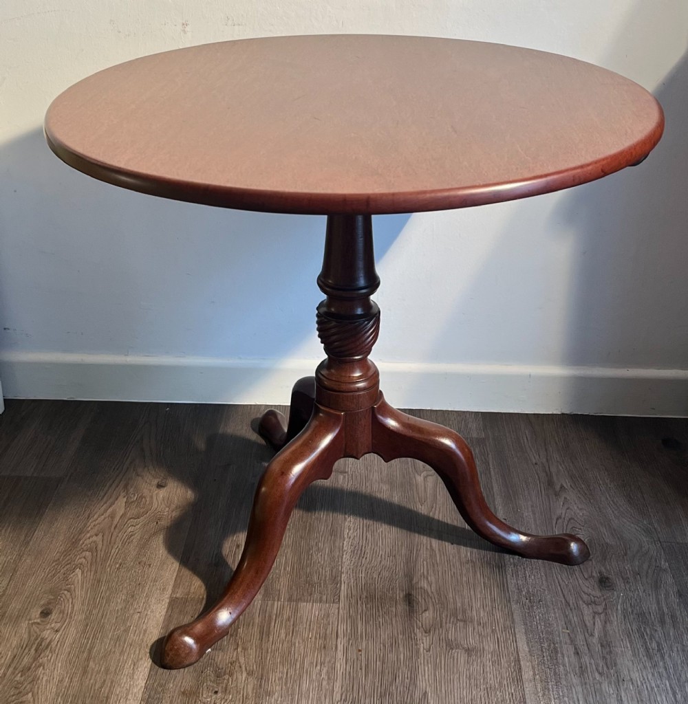 A mahogany tilt-top tripod table shown with its top positioned vertically, revealing a turned central column and cabriole legs. View VI