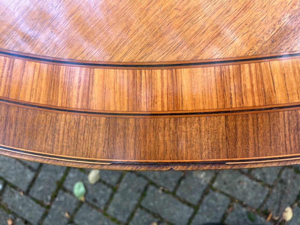 An antique wood tilt-top dining table displaying a circular crossbanded top with inlaid border on a central pedestal base. View V