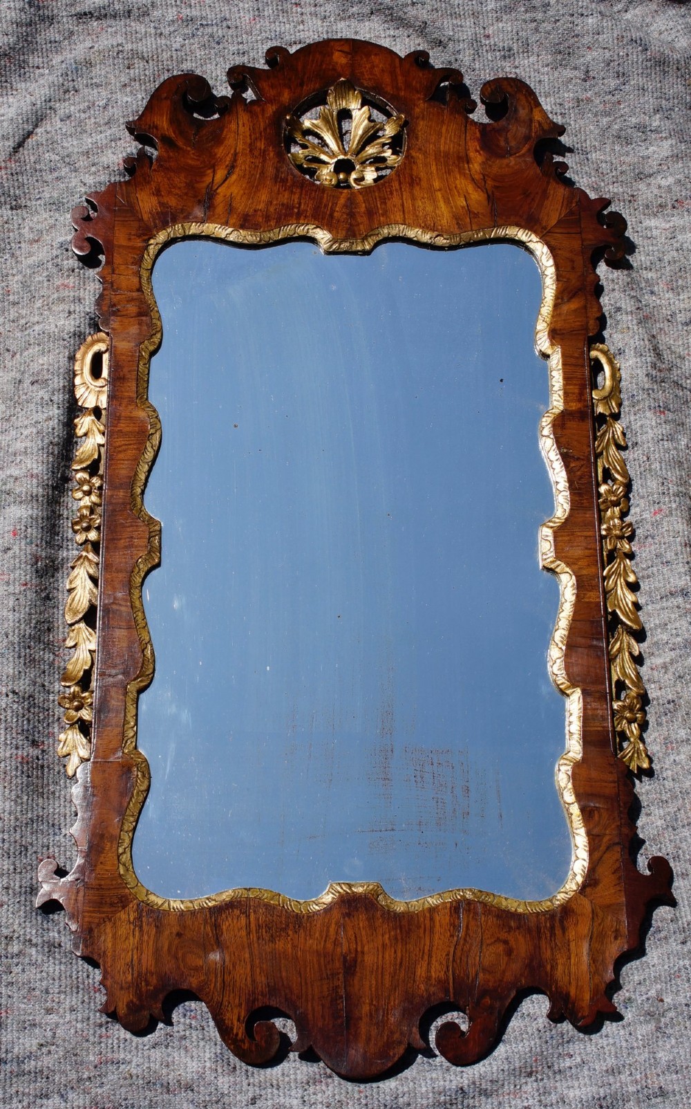 An antique rectangular parcel-gilt walnut wall mirror featuring a fret-cut scrolled frame with gold leaf side garlands and a central carved cresting.