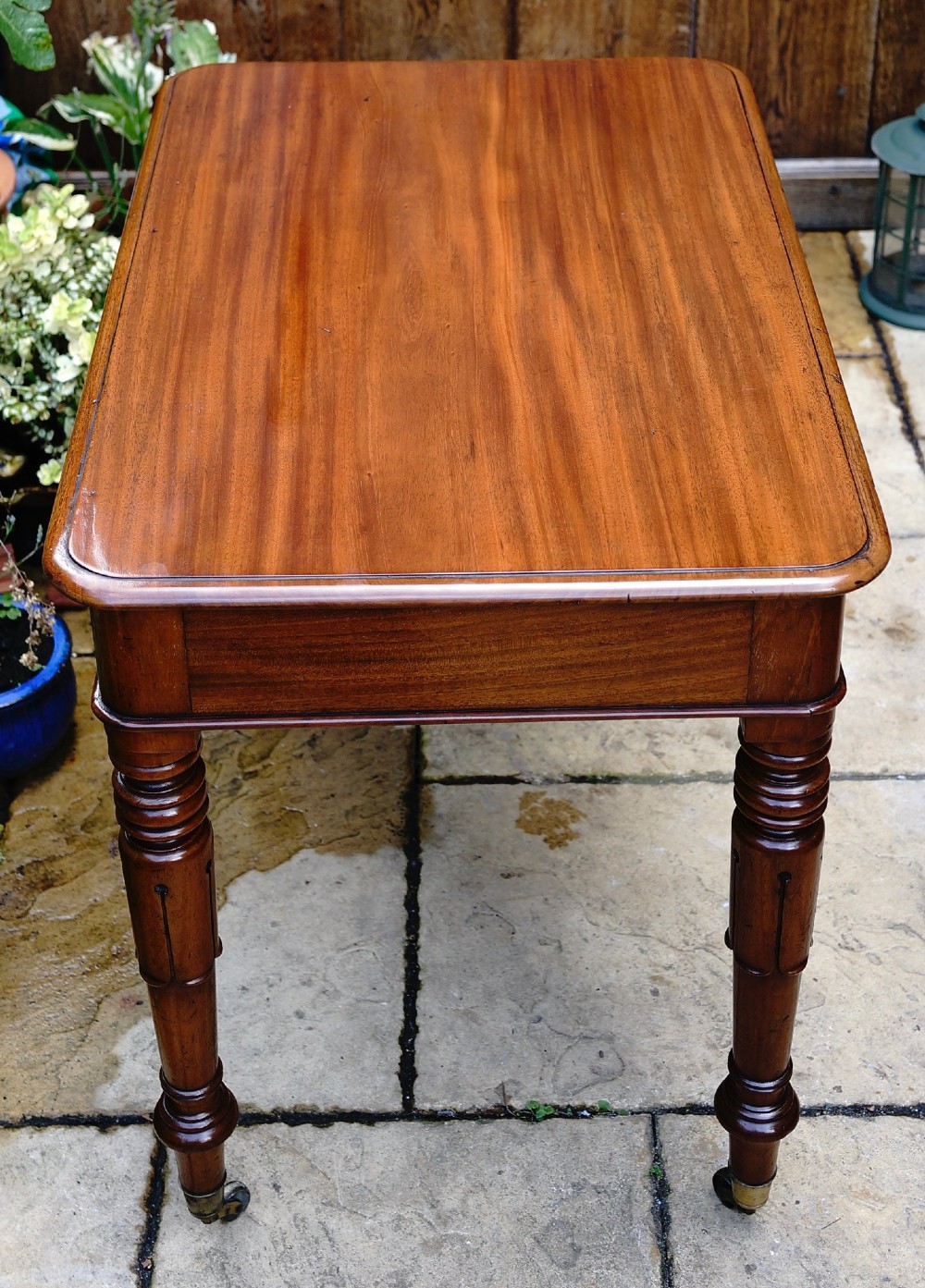 A rectangular mahogany centre table featuring a polished top with rounded corners, dark inlay stringing, a deep apron, and turned legs on brass castors. View V