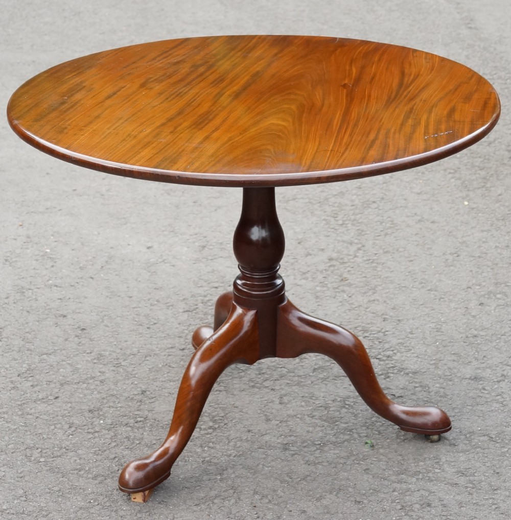 A circular mahogany tripod table featuring a turned baluster stem supported by three cabriole legs.