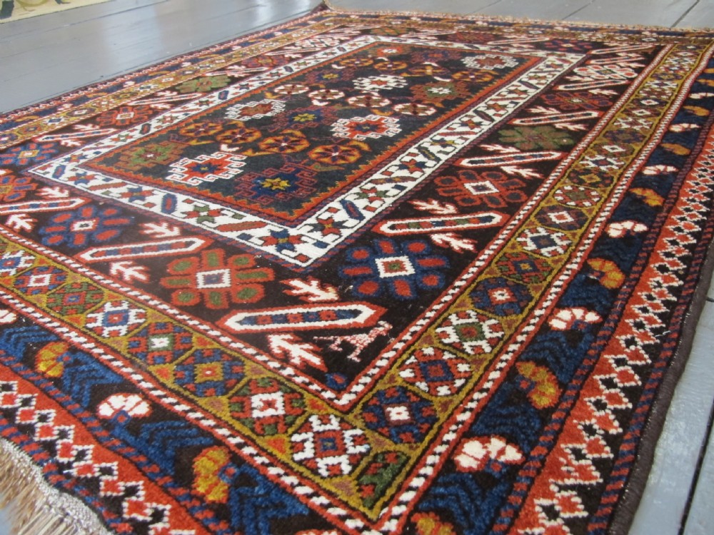 An antique hand-knotted Caucasian Chi-Chi wool area rug featuring intricate geometric motifs and a signature diagonal bar border in navy blue, red, mustard, and green tones.