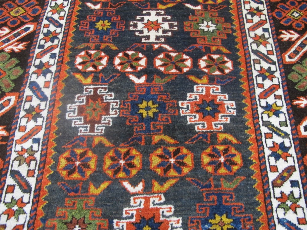 An antique hand-knotted Caucasian Chi-Chi wool area rug featuring intricate geometric motifs and a signature diagonal bar border in navy blue, red, mustard, and green tones. View III