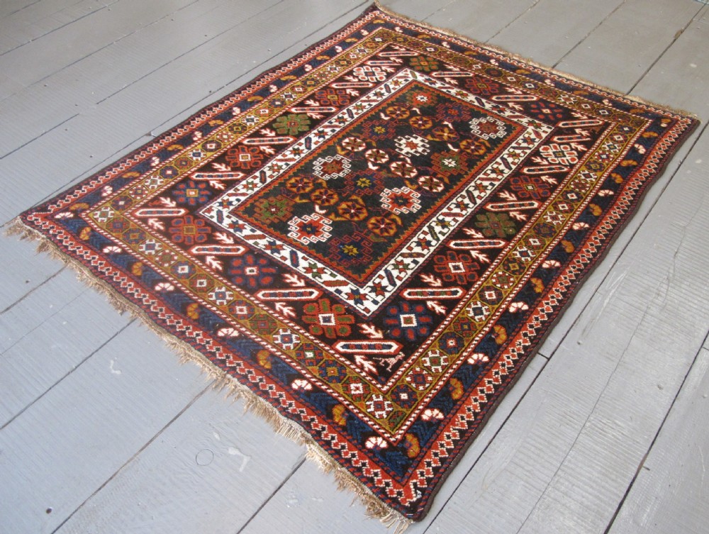 An antique hand-knotted Caucasian Chi-Chi wool area rug featuring intricate geometric motifs and a signature diagonal bar border in navy blue, red, mustard, and green tones. View V
