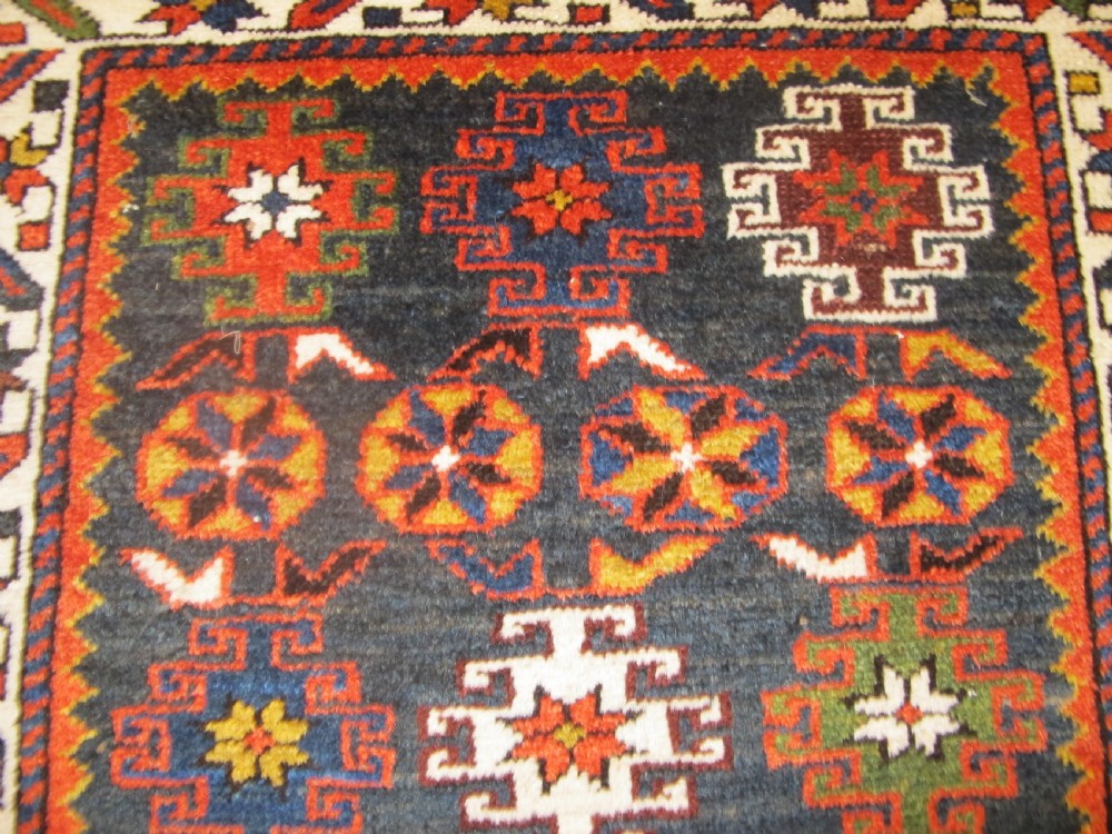 An antique hand-knotted Caucasian Chi-Chi wool area rug featuring intricate geometric motifs and a signature diagonal bar border in navy blue, red, mustard, and green tones. View VI