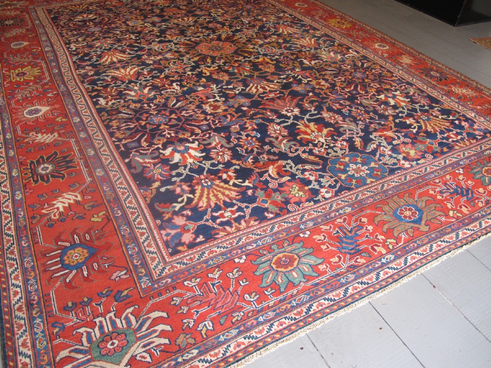 Large rectangular hand-knotted Persian Sultanabad carpet featuring a dark navy floral central field surrounded by a wide terracotta red palmette border. View II
