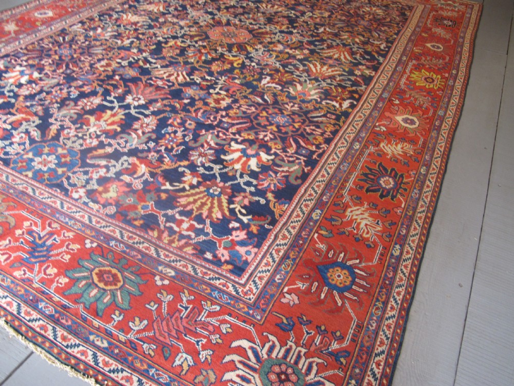 Large rectangular hand-knotted Persian Sultanabad carpet featuring a dark navy floral central field surrounded by a wide terracotta red palmette border. View III