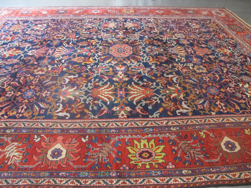 Large rectangular hand-knotted Persian Sultanabad carpet featuring a dark navy floral central field surrounded by a wide terracotta red palmette border. View VI