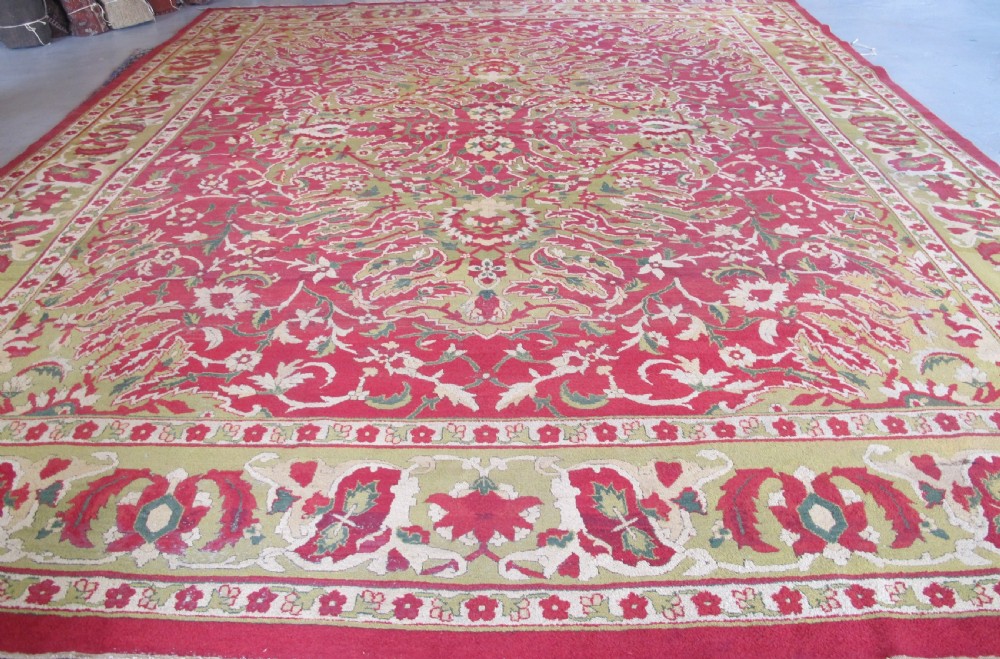 A large hand-knotted wool Amritsar carpet featuring a crimson red field decorated with olive green, cream, and pink floral vine arabesques.