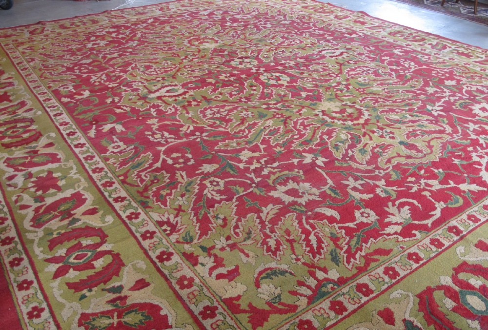 A large hand-knotted wool Amritsar carpet featuring a crimson red field decorated with olive green, cream, and pink floral vine arabesques. View V