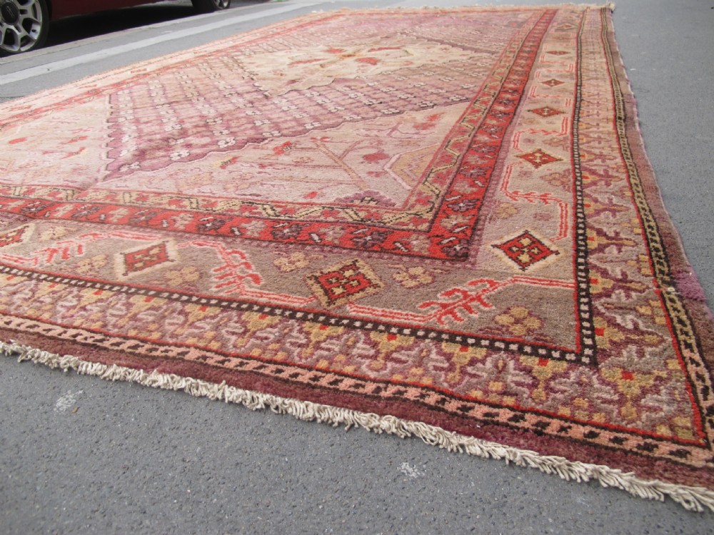 A hand-knotted antique Khotan wool carpet featuring muted rose, terracotta, and beige tones with a geometric lattice pattern and detailed border.