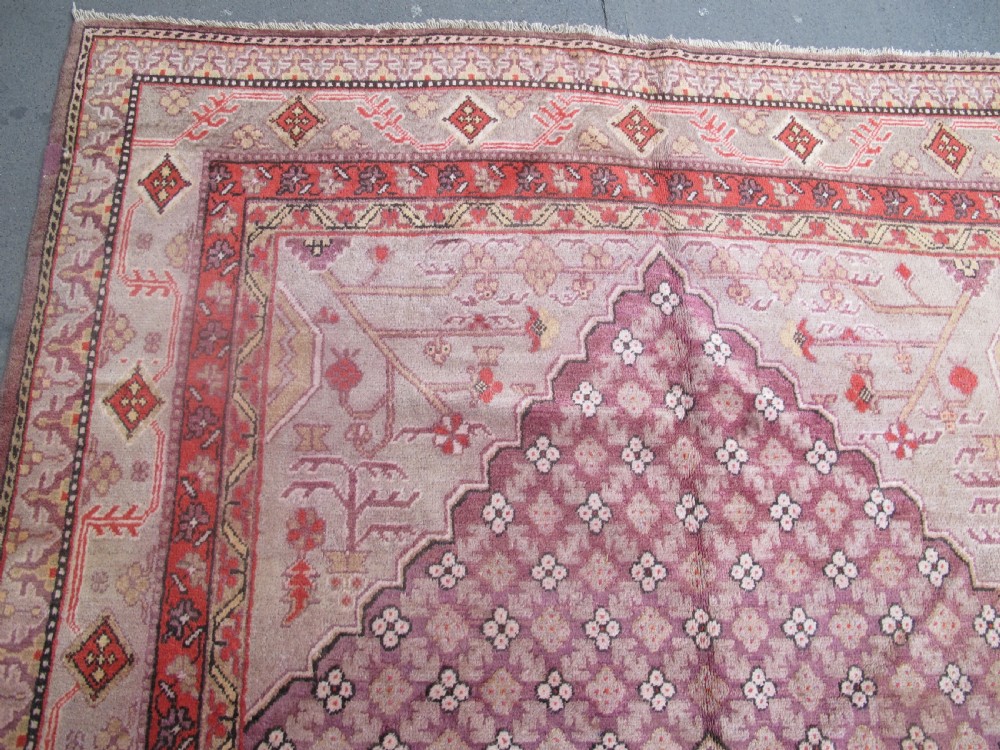 A hand-knotted antique Khotan wool carpet featuring muted rose, terracotta, and beige tones with a geometric lattice pattern and detailed border. View III