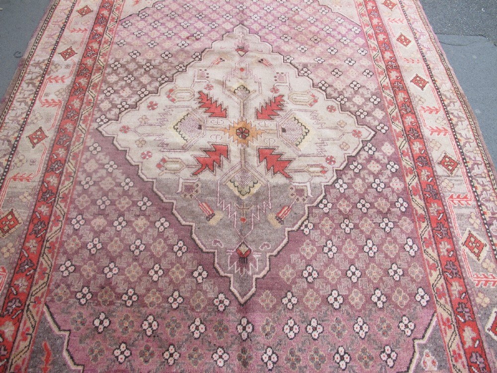 A hand-knotted antique Khotan wool carpet featuring muted rose, terracotta, and beige tones with a geometric lattice pattern and detailed border. View IV