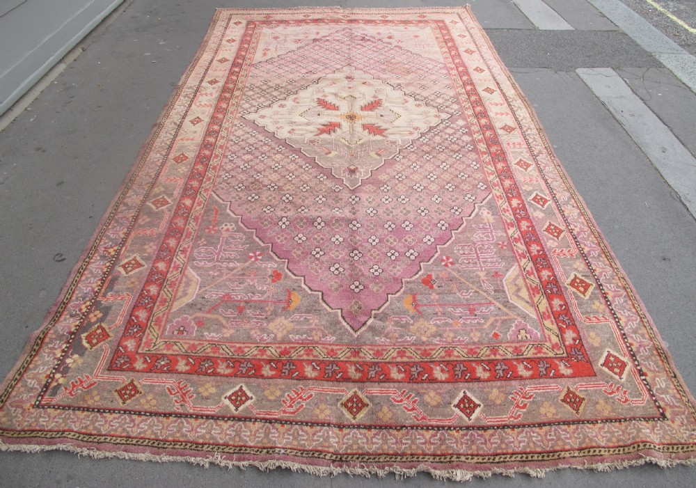 A hand-knotted antique Khotan wool carpet featuring muted rose, terracotta, and beige tones with a geometric lattice pattern and detailed border. View V