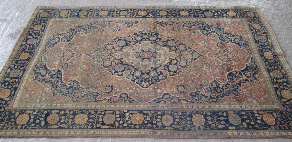 An antique Persian Mohtasham Kashan hand-knotted wool rug featuring a central floral medallion on a terracotta field with a broad navy blue border.