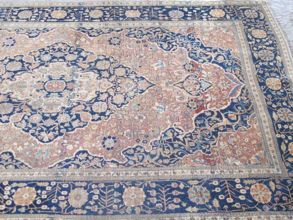 An antique Persian Mohtasham Kashan hand-knotted wool rug featuring a central floral medallion on a terracotta field with a broad navy blue border. View IV