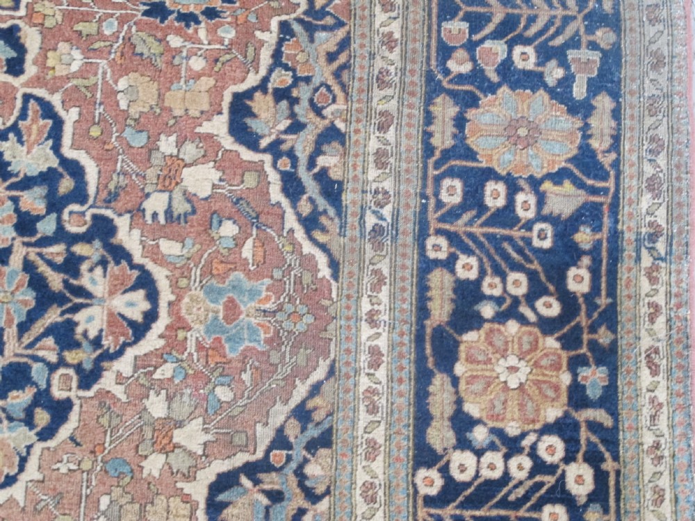 An antique Persian Mohtasham Kashan hand-knotted wool rug featuring a central floral medallion on a terracotta field with a broad navy blue border. View V