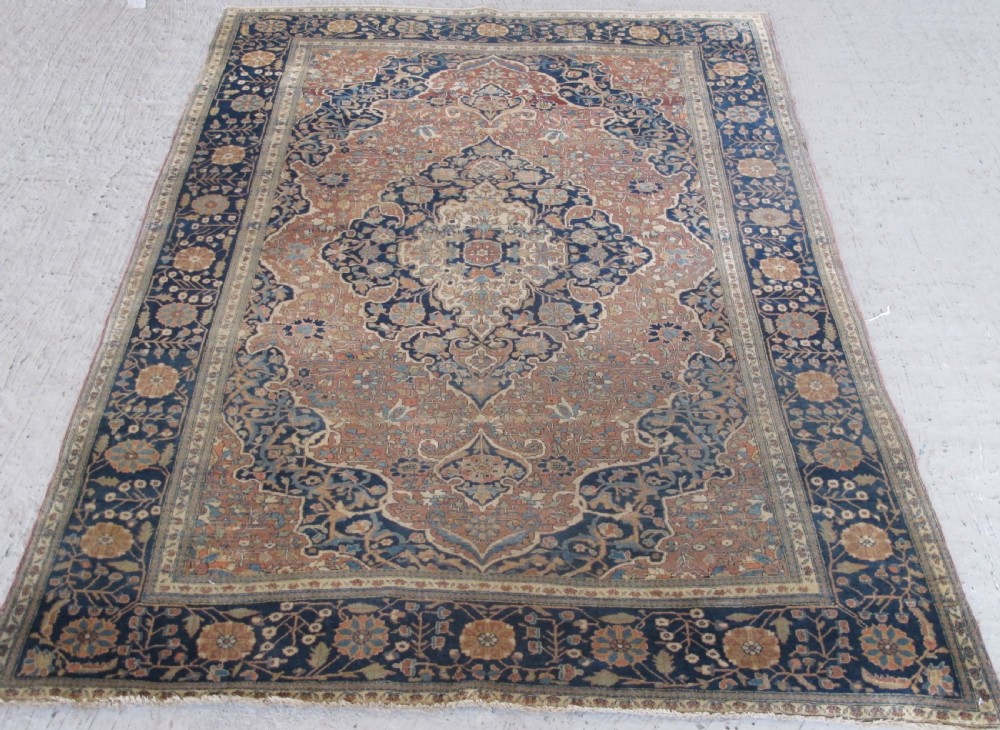 An antique Persian Mohtasham Kashan hand-knotted wool rug featuring a central floral medallion on a terracotta field with a broad navy blue border. View VII