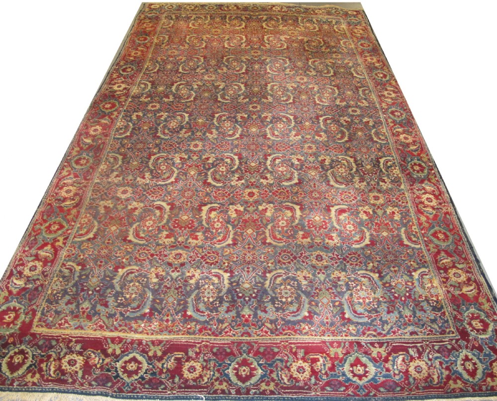 A large late 19th-century hand-knotted Agra wool carpet featuring intricate scrolling botanical motifs in crimson red, blue, and cream with a wide decorative border.
