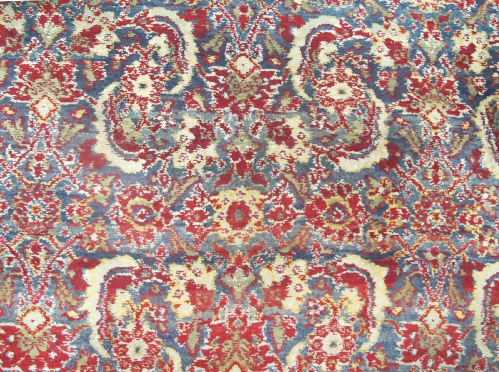 A large late 19th-century hand-knotted Agra wool carpet featuring intricate scrolling botanical motifs in crimson red, blue, and cream with a wide decorative border. View IV