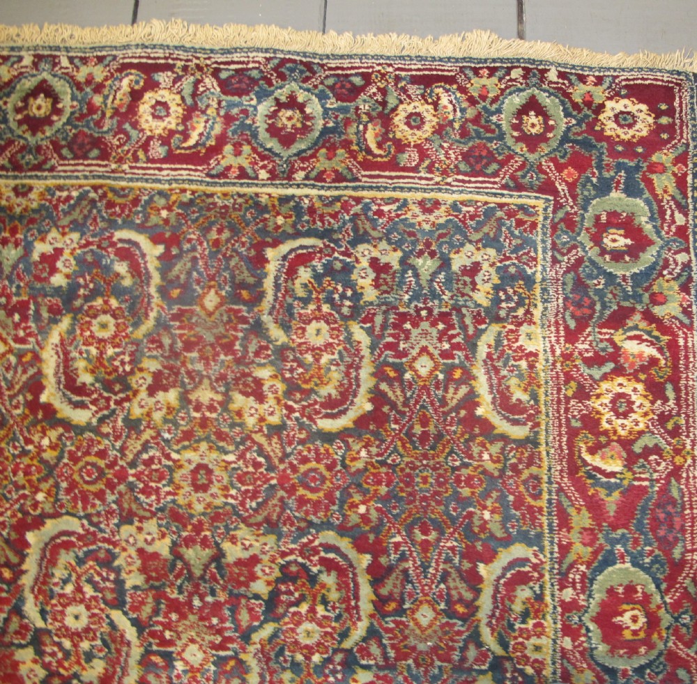 A large late 19th-century hand-knotted Agra wool carpet featuring intricate scrolling botanical motifs in crimson red, blue, and cream with a wide decorative border. View V